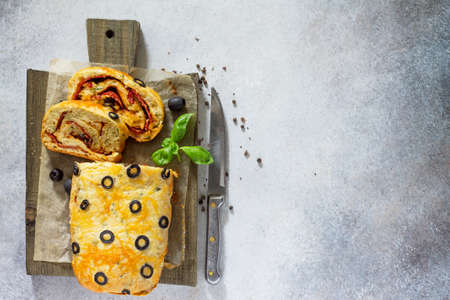Italian cake pizza with salami, cheese, herbs, olives and sun-dried tomatoes. Top view with copy space on a gray stone table. Italian food background.の写真素材