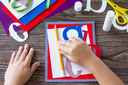 The child glues the details of the application. Greeting card with a pencil and letters for the new...