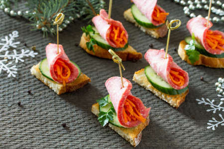 Appetizer canape on crispy bread with cucumber, carrots and sausage. Beautiful Christmas and New Year's food background. Selective focus.の写真素材