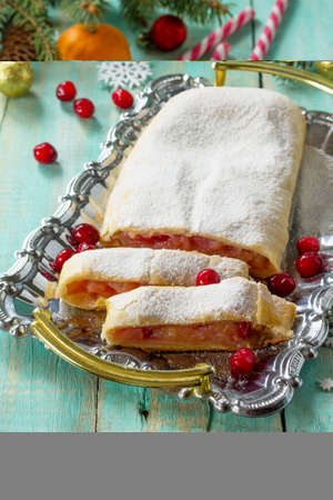 Homemade apple strudel with fresh apples, cranberries and sugar powder on the festive Christmas table. Apple strudel in a country style.の写真素材