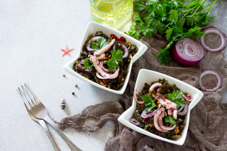 Home snack on a gray stone or slate background. Salad with octopus and sea cabbage. The concept of...