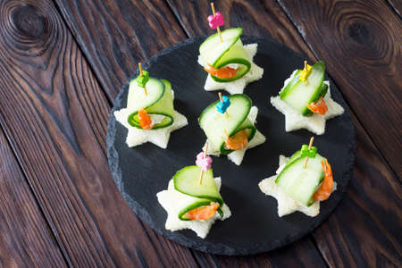 Appetizer canape with white bread, cucumber, ricotta and king prawns on a wooden table.の写真素材