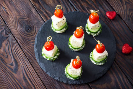 Appetizer canape with white bread, feta cheese, cucumber and cherry tomatoes on a wooden table.の写真素材