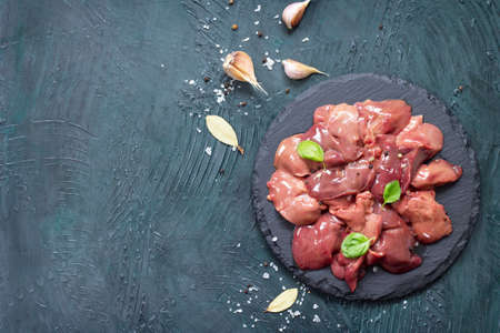 Raw chicken liver on a slate board and spices a gray stone background. Top view with copy space.