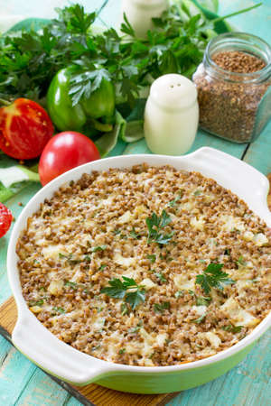 Fish casserole with buckwheat and various greens and vegetables on a kitchen wooden table.の写真素材