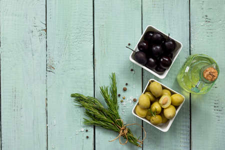 Wooden background with  black olives, green olives, olive oil, fresh rosemary and spices. Flat lay. Top view with copy space.の写真素材
