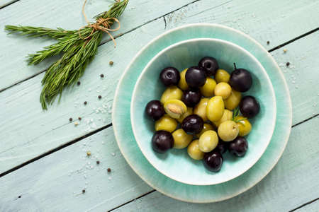 Wooden background with  black olives, green olives, olive oil, fresh rosemary and spices. Top view with copy space.の写真素材