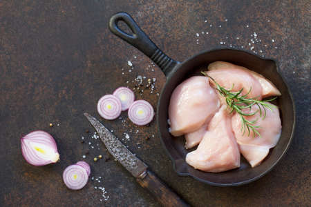 Fresh meat. Raw chicken fillet on a cast-iron frying pan, spices and fresh rosemary on the kitchen table. Top view with a copy.の写真素材