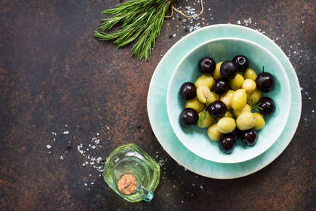 Culinary background. Olives, green olives with olive oil, fresh rosemary and spices on a stone or slate background. Top view with a copy.の写真素材