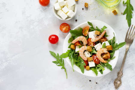 Festive appetizer. Salad with shrimps, feta cheese, arugula, cherry tomato and sesame on a stone or slate background. Top view.の写真素材