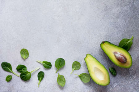 Avocado halves and baby spinach leaves on concrete, stone or slate background. Dietary food, concept of vegetarian food. Top view with copy space.の写真素材