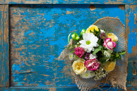 A wedding story or background Mother's Day. Basket bouquet of roses and chrysanthemums on a vintage wooden background. Copy space, top view, flat lay.の写真素材