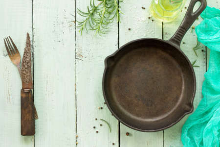 Culinary background. Cast-iron frying pan and fresh rosemary on the kitchen wooden table. Copy space, top view flat lay background.の写真素材
