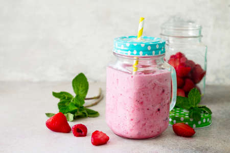 Mason jar mugs with fresh berry smoothies and fresh strawberries and raspberries on a gray stone or slate background. The concept of proper nutrition and health or detoxification. Copy space.の写真素材