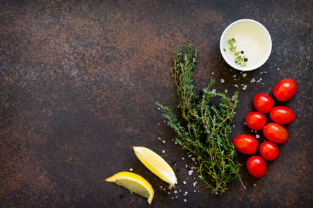 Ingredients for cooking on a dark stone table - thyme, cherry tomato, olive oil and lemon. Copy space, top view flat lay background.の写真素材