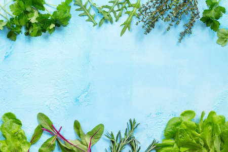Food background. Various summer green fresh herbs - parsley, lettuce, rosemary, thyme, arugula and spinach on a blue stone table. Copy space, top view flat lay background.の写真素材