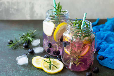 Lemonade or cocktail with blueberries and rosemary, cold refreshing drink with ice on dark concrete or stone table. Copy space.の写真素材