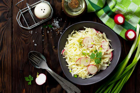 Summer salad with fresh cabbage and radish dressed with olive oil on a wooden table. Healthy proper nutrition. Copy space, top view flat lay background.の写真素材