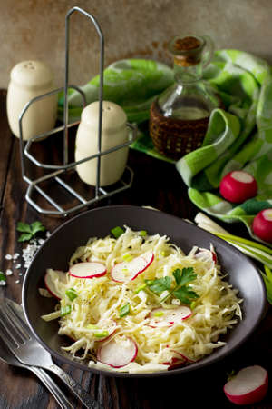 Diet, concept of vegetarian food. Summer salad with fresh cabbage and radish dressed with olive oil on a wooden table. Healthy proper nutrition.の写真素材