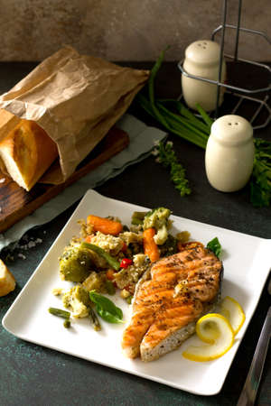 Grilled salmon steak, couscous and vegetables (string beans, brussels sprouts, carrots, sweet peppers, tomatoes) on stone or concrete table. Healthy proper nutrition. Copy space.の写真素材