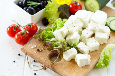 Feta cheese and black olives, cooking qreek salad with fresh vegetables on a white wooden table. の写真素材