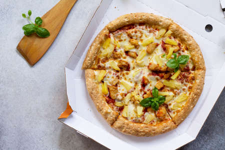 Pizza Hawaiian in a cardboard box on a light stone or concrete background. Space for text. Top view....