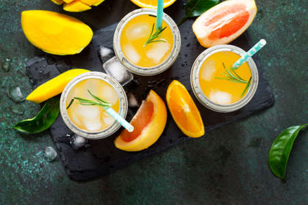 Fresh refreshing summer drinks. Multifruit drinks of citrus and mango with ice, smoothies on a dark stone background. Copy space, top view flat lay background.の写真素材