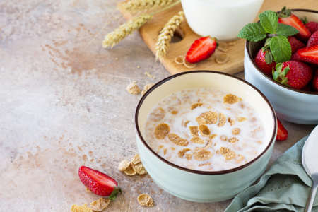 Healthy breakfast - whole grain flakes, milk and fresh strawberries on stone or slate background....
