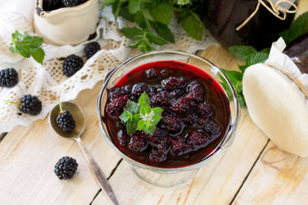 Homemade jam. Glass jar with blackberry and mint on a wooden table. Preserved berry. Copy space.