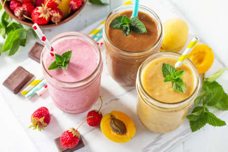 Strawberry, chocolate and apricot smoothie on a white wooden background. Healthy juicy vitamin drink...