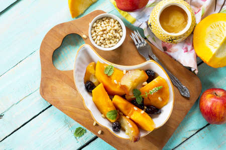 Pumpkin baked with apples, prunes and spices in a bowl on a wooden table. Flat flay, top view with copy space.の写真素材