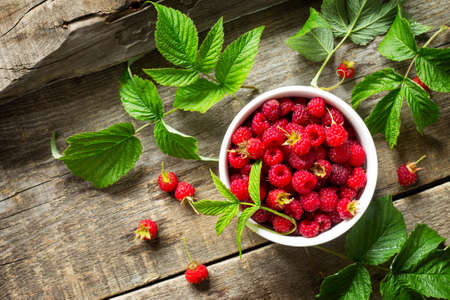 Fresh sweet raspberries in a ceramic bowl on a wooden table. The concept of nutrition health or...