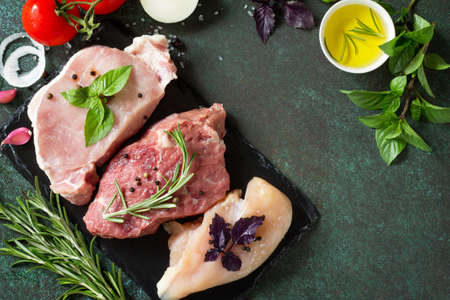 Fresh raw meat. Different types of raw pork meat, chicken fillet and beef with vegetables and herbs on dark wooden background. Top view. Copy space.の写真素材