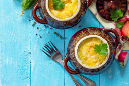 Potatoes and red fish with cream and cheese bake in clay pots in the kitchen wooden background....