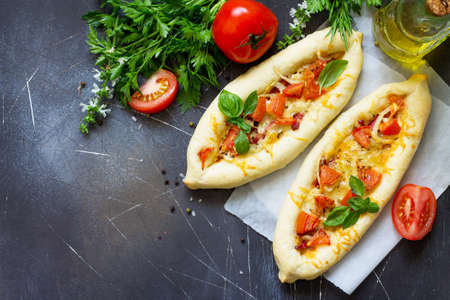 Delicious homemade Greek oval pizza with salami, tomato, onion and cheese on a dark stone...