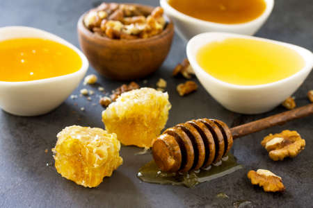 Natural Various Honey and Nuts. Honey in glass jar and dipper, Sweet Honeycombs on dark stone table.