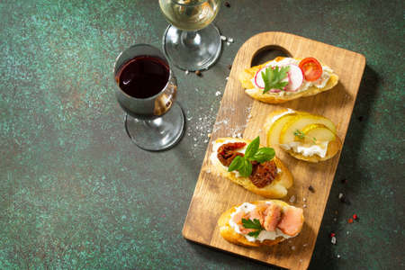 Italian Antipasti snacks set for Wine. Variety Brushetta with Soft Cheese, Pear, Radish, Salmon and Dried Tomatoes served on a rustic wooden board on a stone table. Copy space.の写真素材