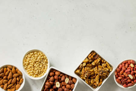 Various nuts in a ceramic bowl (walnut, almonds, pine nuts, hazelnuts) on a light stone table. The concept of a healthy dessert.Top view flat lay background. Copy space.の写真素材