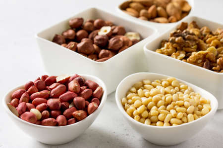 Various nuts in a ceramic bowl (walnut, almonds, pine nuts, hazelnuts) on a light stone table. The concept of a healthy dessert.の写真素材