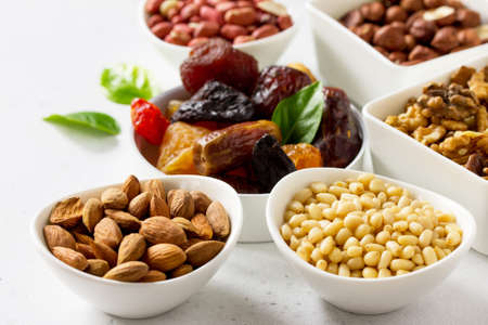 Various Nuts in a ceramic bowl and Dried Fruits on a light stone table. The Concept of a Healthy...