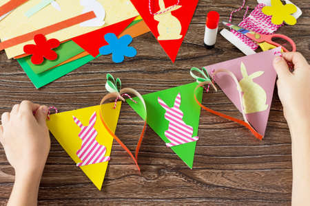 The child folds details festive Easter garland on a wooden background. Project of children's...