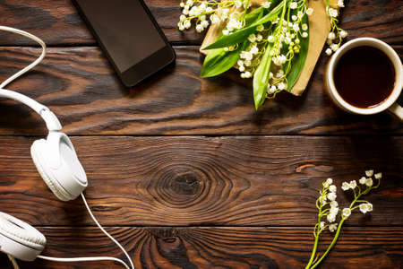 Springtime. Smartphone, lilies of the valley, headphones and coffee cup on a wooden table. Flat lay, top view background. Copy space.の写真素材