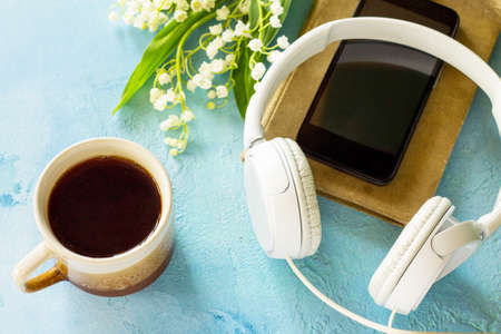 Springtime. Smartphone, lilies of the valley, headphones and coffee cup on stone table.