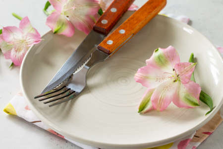 Spring or Mother's Day table setting. Plate, cutlery and napkin on white stone table. Copy space.