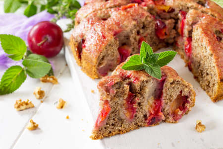 Delicious dessert plum pie, sweet delicious holiday plums cake with nuts on the white kitchen table.の写真素材
