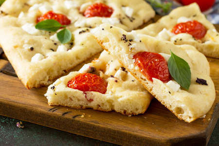 Traditional Italian Focaccia with rosemary, tomatoes and feta - close-up homemade flat bread...
