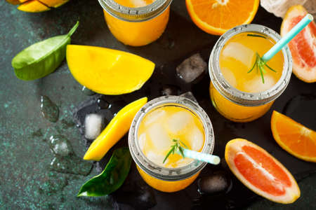 Refreshing summer cocktails made of citrus and mango, cold drink with ice on a dark stone...