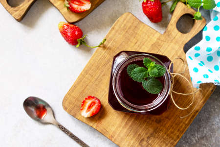 Homemade preservation. Fresh strawberry berries and strawberry berry syrup on a light stone table....