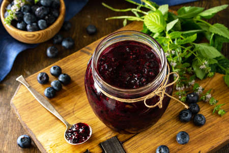 Organic Homemade Preserves. Blueberry jam in a jar and fresh blueberries on rustic wooden table....