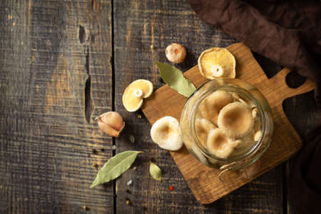 Fermented food: Mushroom preservation. Home preservation of products: glass jars with pickled mushrooms with spices on a rustic wooden table.  Top view flat lay. Free space for your text.の写真素材